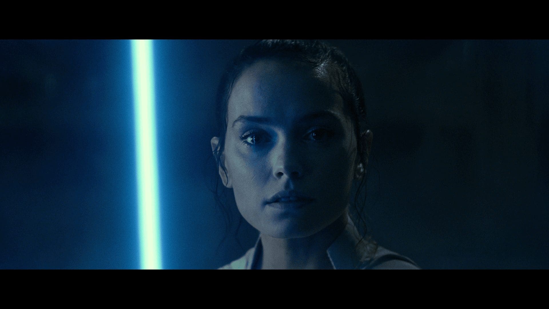 Rey bathed in blue saber light, listening